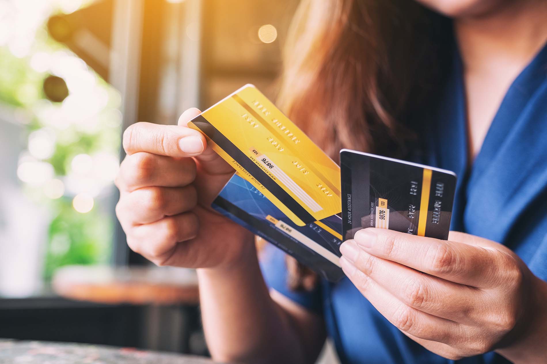 Close-up of a woman holding three credit cards fanned out, deciding which card is the best.