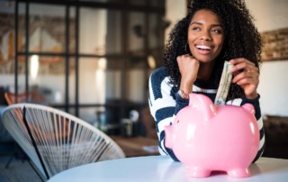 Pretty, young, black woman with curly hair putting a 20 dollar bill into a piggy bank.