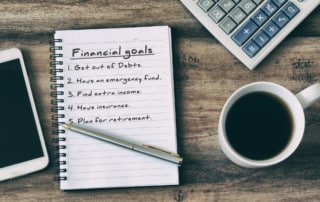 Aerial view of a notebook with financial goals written on it, a coffee cup, calculator, and pen
