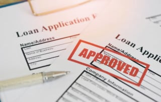 Paper loan applications with the word approved stamped in red on one of them