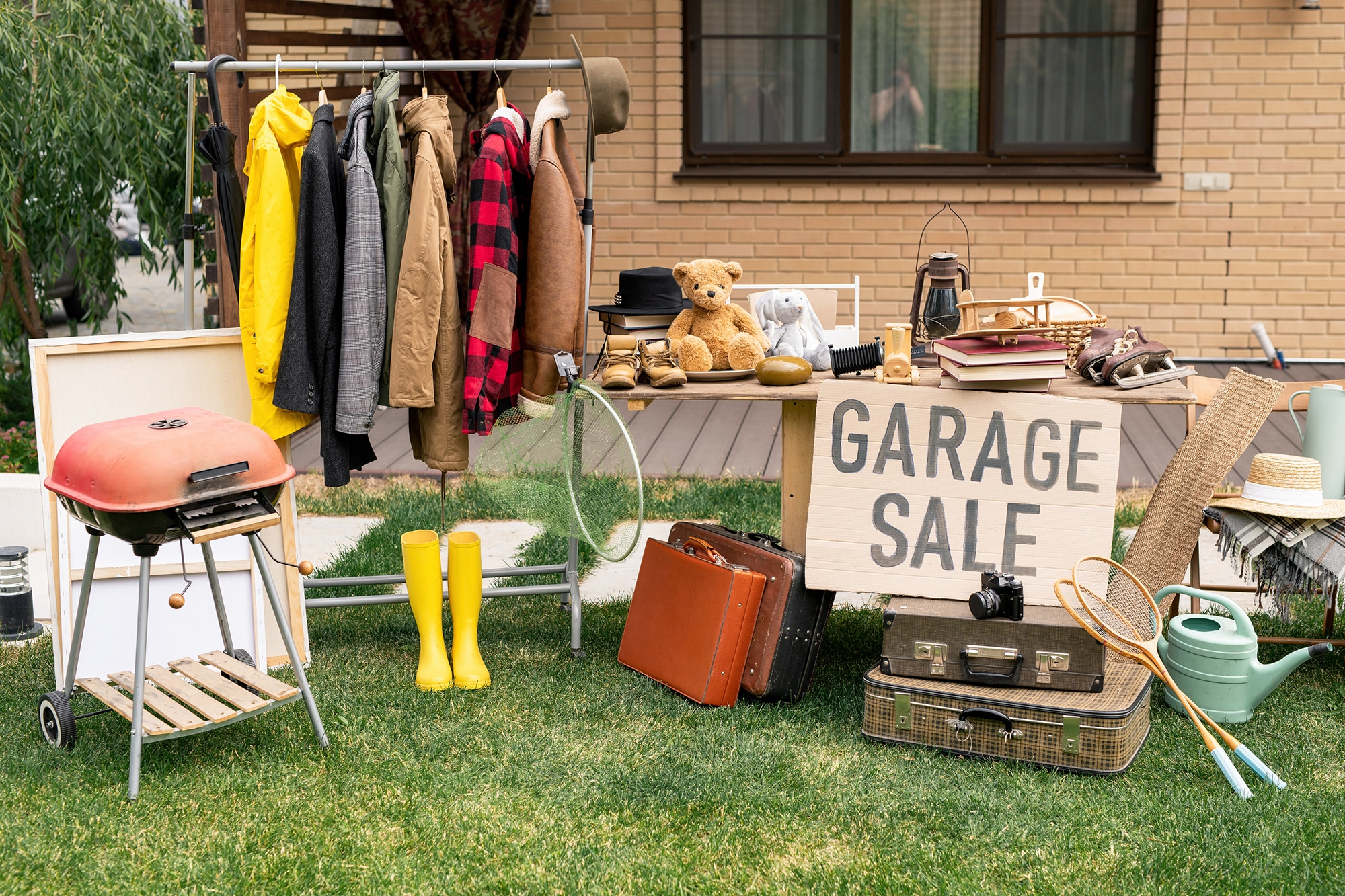 Picture showing items at a garage sale, including jackets, a grill, and a teddy bear.