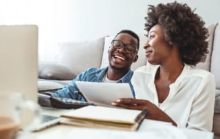 Black man and woman, a couple, sitting on the floor looking and paperwork reviewing finances