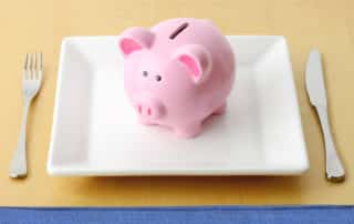 Pink piggy bank sitting on a white plate with a fork and knife on either side