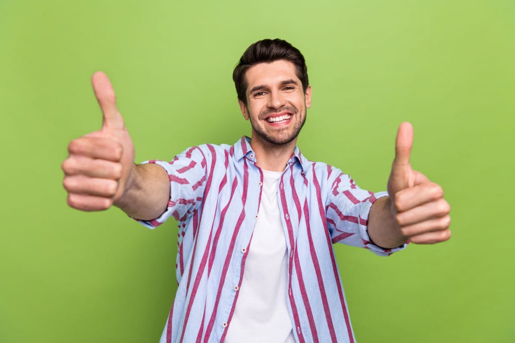 Photo of friendly funny man with stylish haircut dressed striped shirt showing thumbs up to you isolated on green color background
