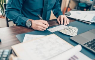person writing a paper check with cash stting on desk