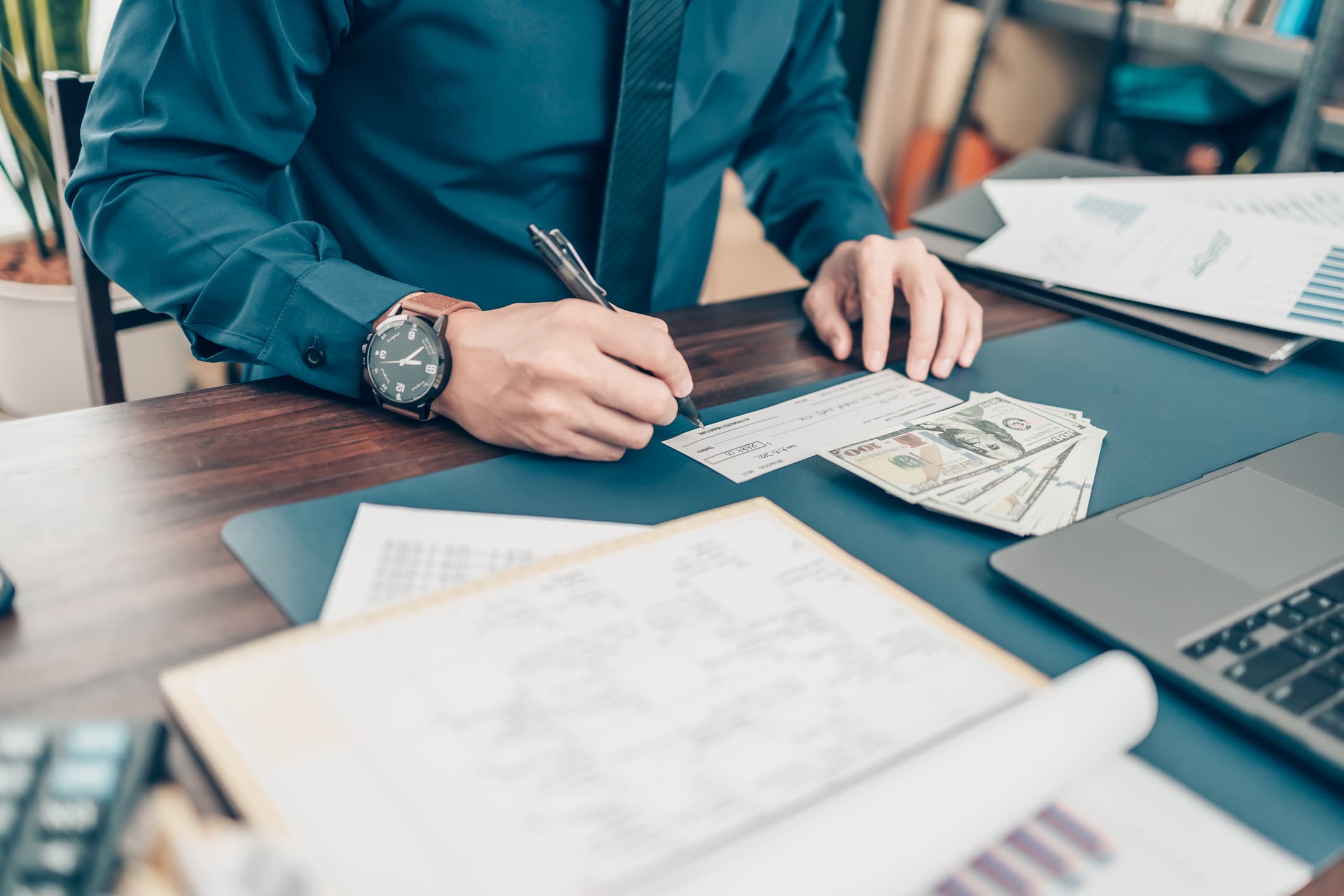 person writing a paper check with cash stting on desk